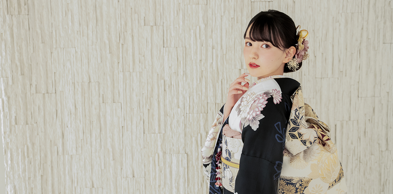 薄緑色の振袖を着て、木蓮の花を手に持つ女性の横顔。落ち着いたグレーの背景に影が映し出されている。