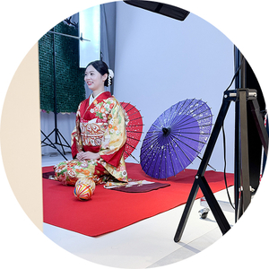 本格的な撮影スタジオで、和傘を背景に赤い振袖姿で微笑む女性