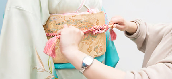 専門スタッフによる丁寧な着付け。振袖の帯締めを整えている手元のアップ