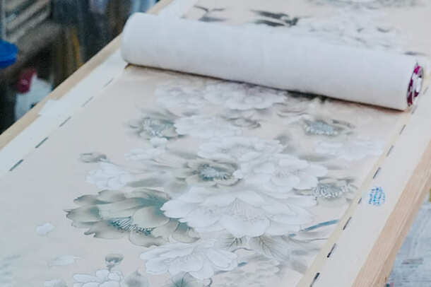 作業台に張られた反物。淡い地に白と薄墨の大きな花が描かれ、奥には白い生地が巻かれている